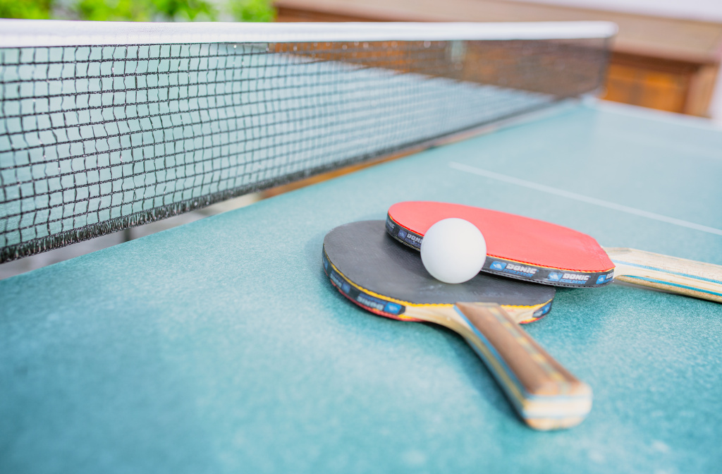 Tischtennisnetz mit Schlägern und weißem Ball auf einer blauen Platte